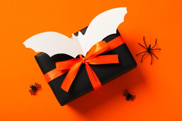 Gift box decorative spiders and paper bat on orange background top view