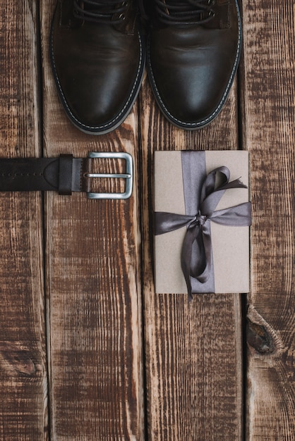 Gift box for father's day with men's accessories belt and leather shoes on a wooden table. Flat lay.