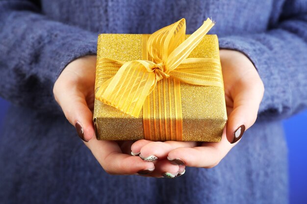 Gift box in female hand on color background