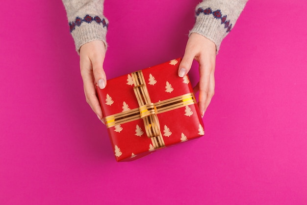 Gift box in female hands on pink background