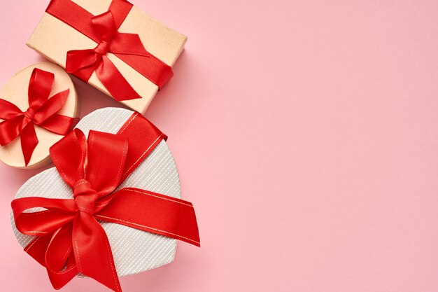 Gift box in the form of heart with a red ribbon on pink background. Valentines day concept postcard. Top view.