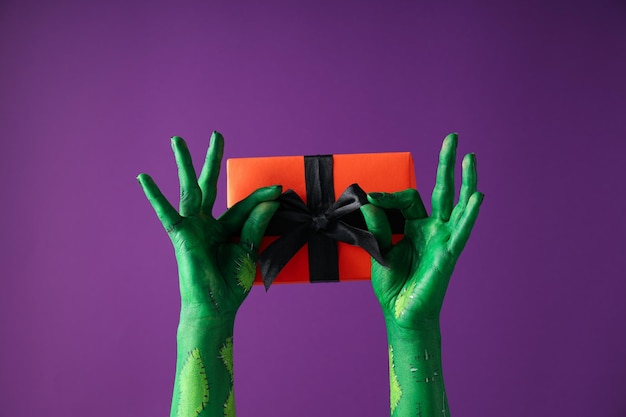 Gift box in green female hand on purple background close up
