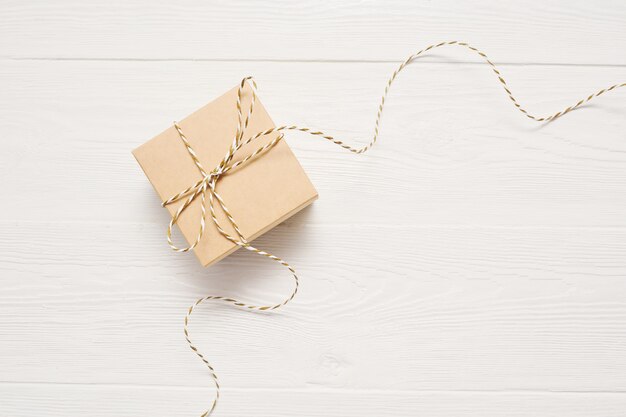 Gift box on kraft paper with a rope bow is on a white wooden table, with place for your text