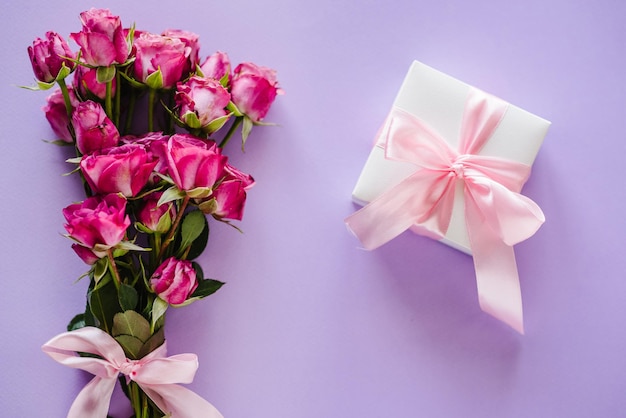 Confezione regalo e rose rosa su sfondo viola cartolina spazio per messaggio di testo concetto di fiori biglietto di auguri per le vacanze per san valentino festa della mamma della donna buon compleannovista dall'alto