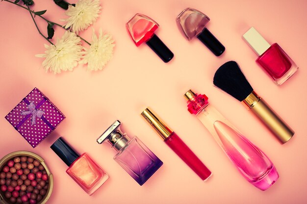 gift box, powder, nail polish, bottles of perfume, lipstick, brush and flowers on a pink background. women cosmetics and accessories. top view. color toning.