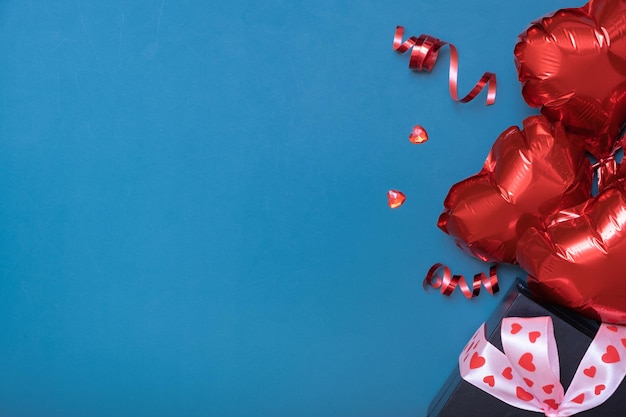 Подарочная коробка и красные воздушные шары в форме сердца на синем фоне Поздравительная открытка на День Святого Валентина Копией пространства