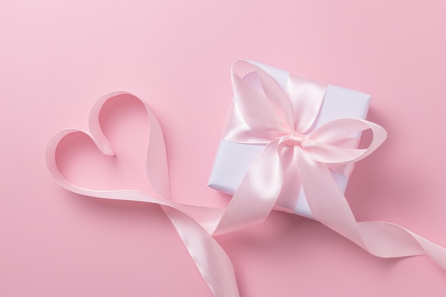 Gift box and ribbon in the shape of a heart on a pink surface. Valentine's day concept.