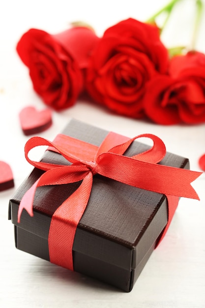 Gift box rose flowers and decorative hearts on light wooden background