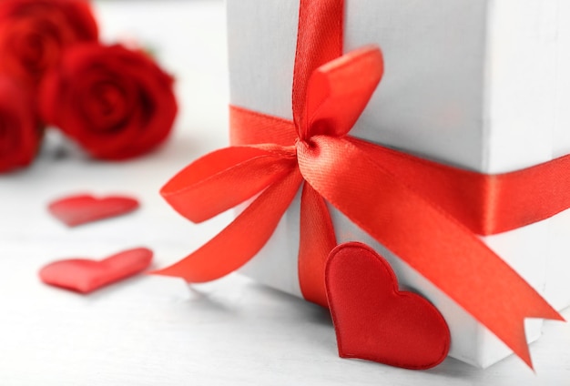 Gift box rose flowers and decorative hearts on light wooden background