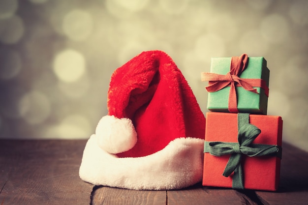 Gift box and santa claus hat on wooden table with bokeh on background