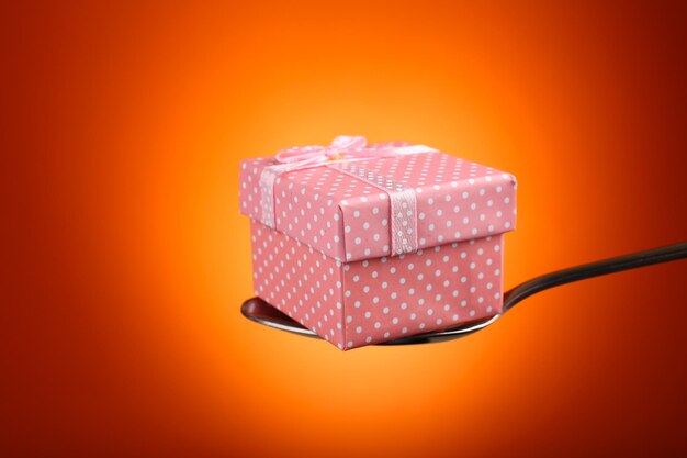 Gift box in silver spoon on orange background