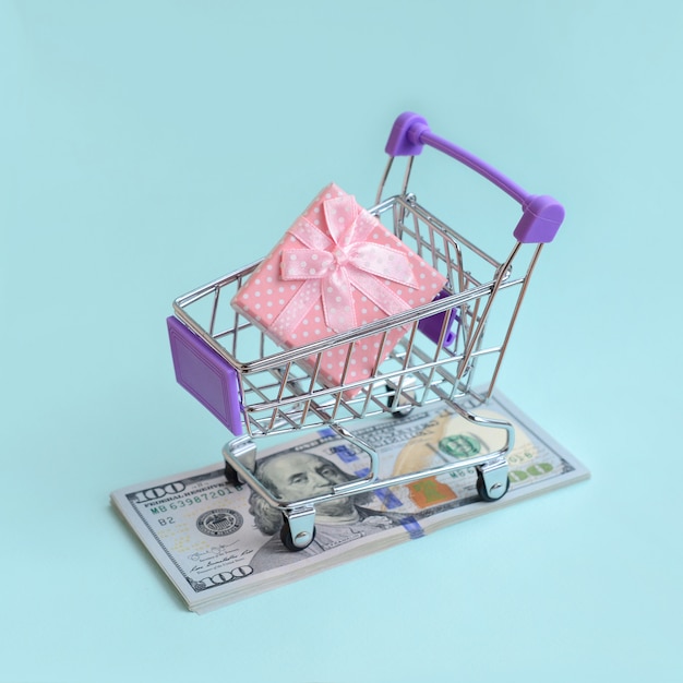 Gift box in a small shopping cart lies on a dollar bills o