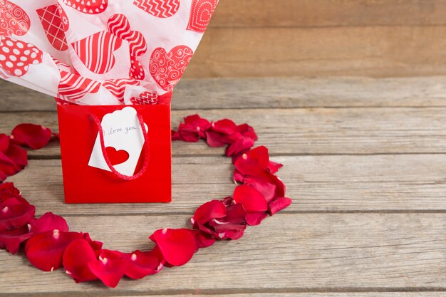 Gift box surrounded by red rose petals place in heart shape