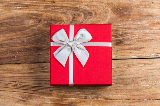 Gift box tied red ribbon with small red hearts printed on it. On old wooden background.