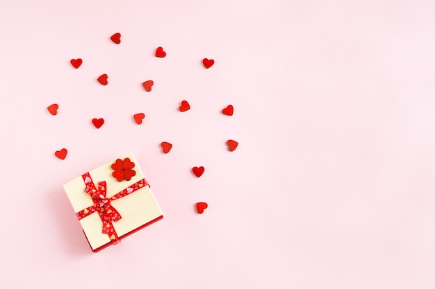 Подарочная коробка, перевязанная лентой с маленькими деревянными красными сердцами, вид сверху на розовом бумажном фоне с копией пространства
