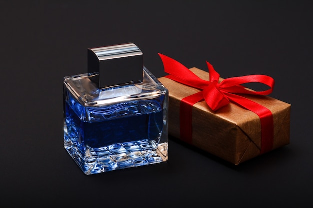Gift box tied with red ribbon and bottle of perfume on black background. Celebration day concept.