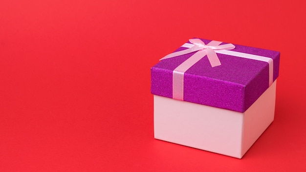 Подарочная коробка перевязана лентой на ярко-красном фоне. Праздничный подарок.