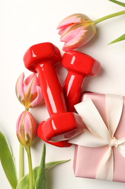 Gift box, tulips and dumbbells on white background