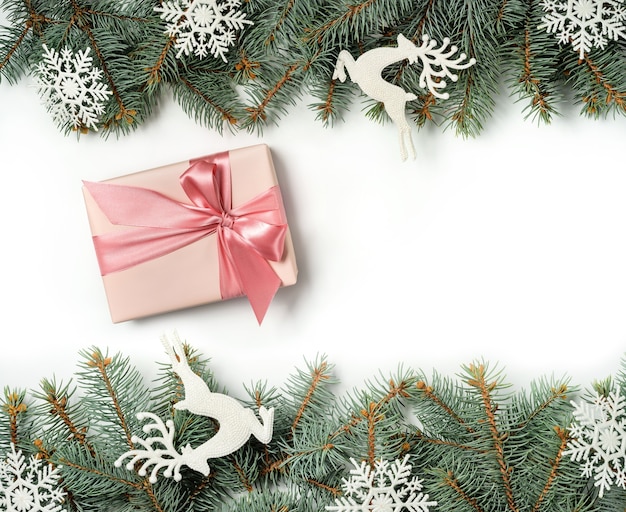 A gift box between two rows of Christmas tree branches decorated with snowflakes and deer figurines.