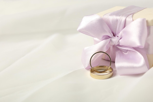 Gift box and wedding rings on light background space for text