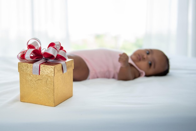 Gift box on white bed with blur of African black skin newborn