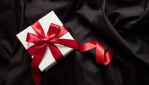 Gift box white with red ribbon on black satin christmas\
valentine day present black friday