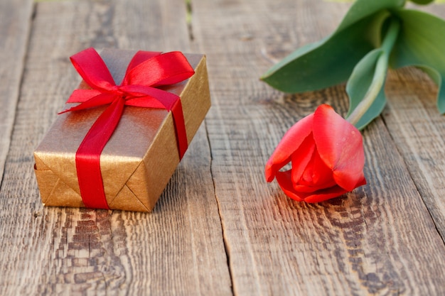 Gift box with beautiful tulip on the wooden background. Concept of giving a gift on holidays. Top view.