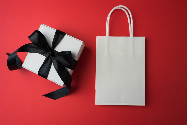 Gift box with black ribbon and shopping bags on red background with copy space Black Friday sale