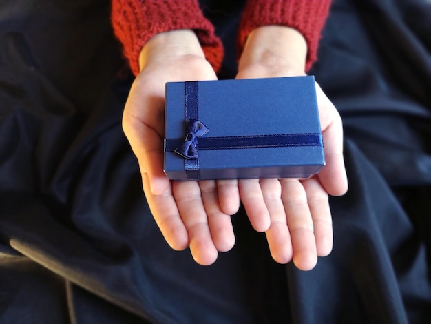 Gift box with a blue bow in childrens hands Black wavelapped fabric in the background