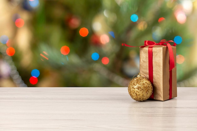 Gift box with a bow a toy ball and blurred twinkling party lights on the background