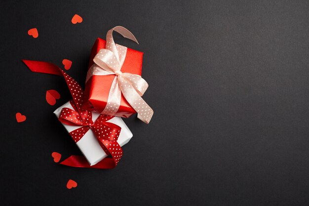 Gift box with bows and red paper hearts on black background with copy space top view Valentines day