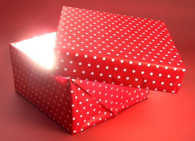 Gift box with bright light on it on red background