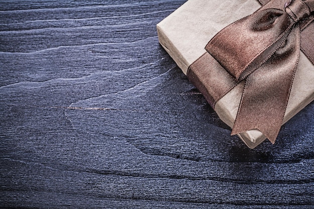 Gift box with brown satin bow on wooden board