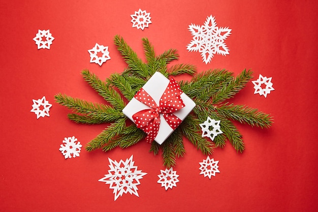 Gift box with Christmas tree branch and white snowflakes on red background top view