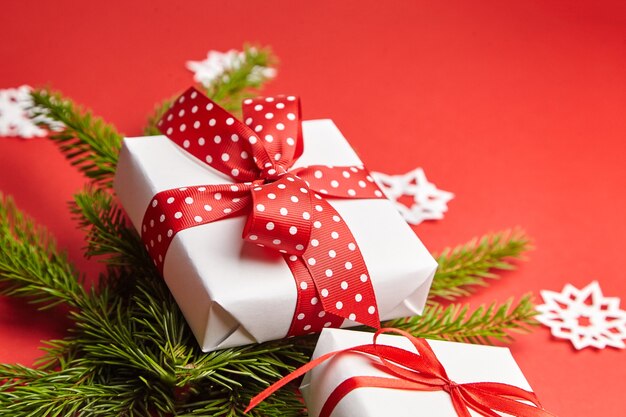 Gift box with Christmas tree branch and white snowflakes on red background