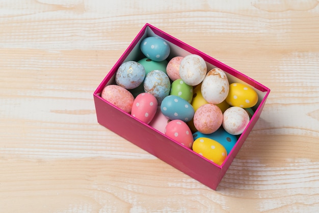 Gift box with colorful brighrt Easter eggs. Wooden background.