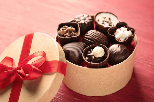 Подарочная коробка с вкусными конфетами на красном деревянном фоне
