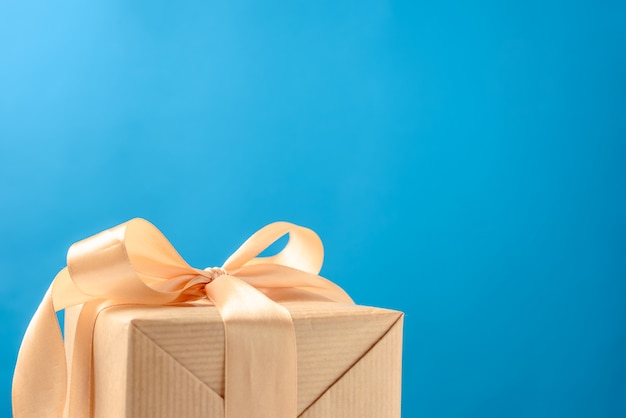 Gift box with gold bow on a blue background, copy space