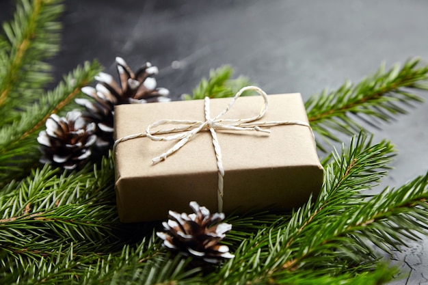 Gift box with green Christmas tree branches and cones on dark background