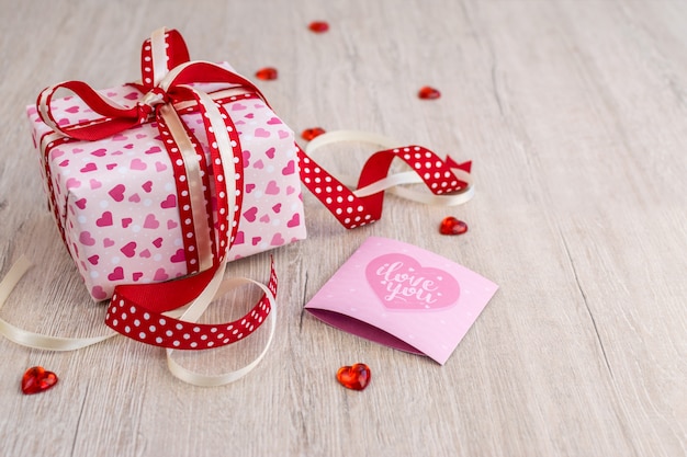 Gift box with hearts and greeting card on wood background