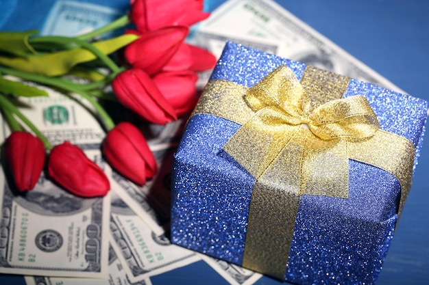 Photo gift box with money and flowers on color wooden table