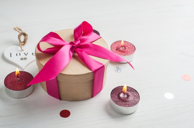 Gift box with pink bow and lit candles