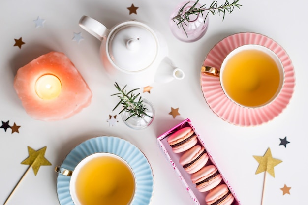 Gift box with pink macaroons among vintage cups of green tea, stars and small vases