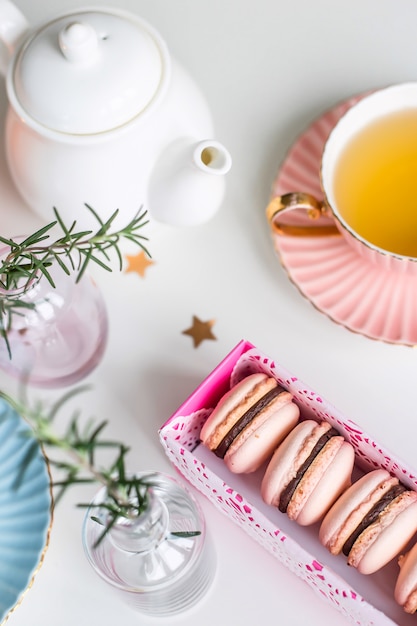 Gift box with pink macaroons among vintage cups of green tea, stars and small vases