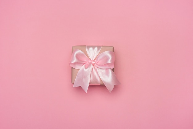 Gift box with pink ribbon bow on pastel pink table.