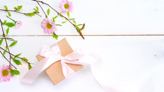 A gift box with a pink ribbon and a pink bow on a white wooden table.