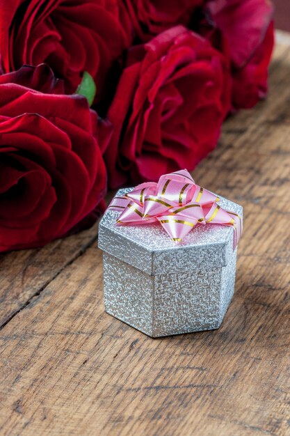 Gift box with pink ribbon and red roses behind