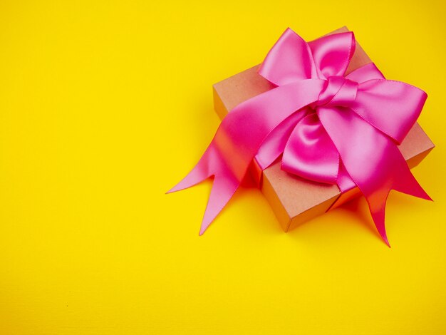 Gift box with pink satin ribbon on yellow background