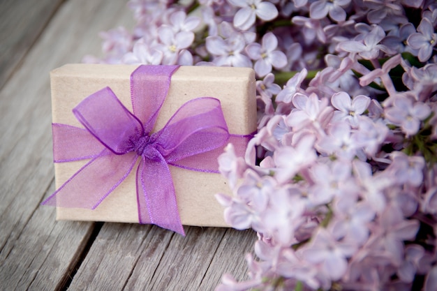 Photo gift box with purple bow and lilac flowers on wood close up