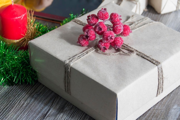 A gift box with red berries packed in kraft paper and tied with linen twine on a wooden background